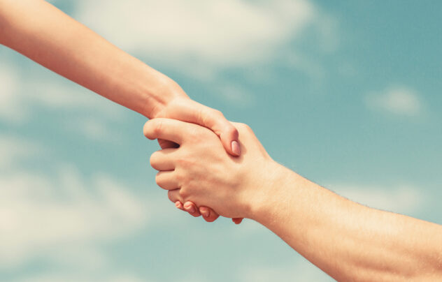 Giving a helping hand. Lending a helping hand. Solidarity, compassion, and charity, rescue. Hands of man and woman on blue sky background.