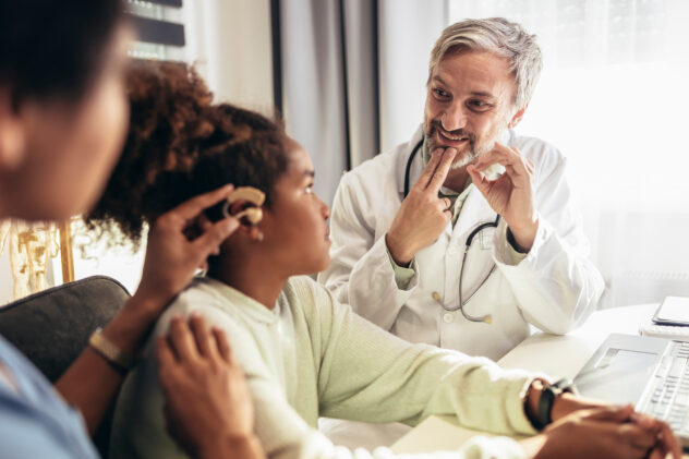 Smiling deaf african american girl with ear implant at doctor's office.